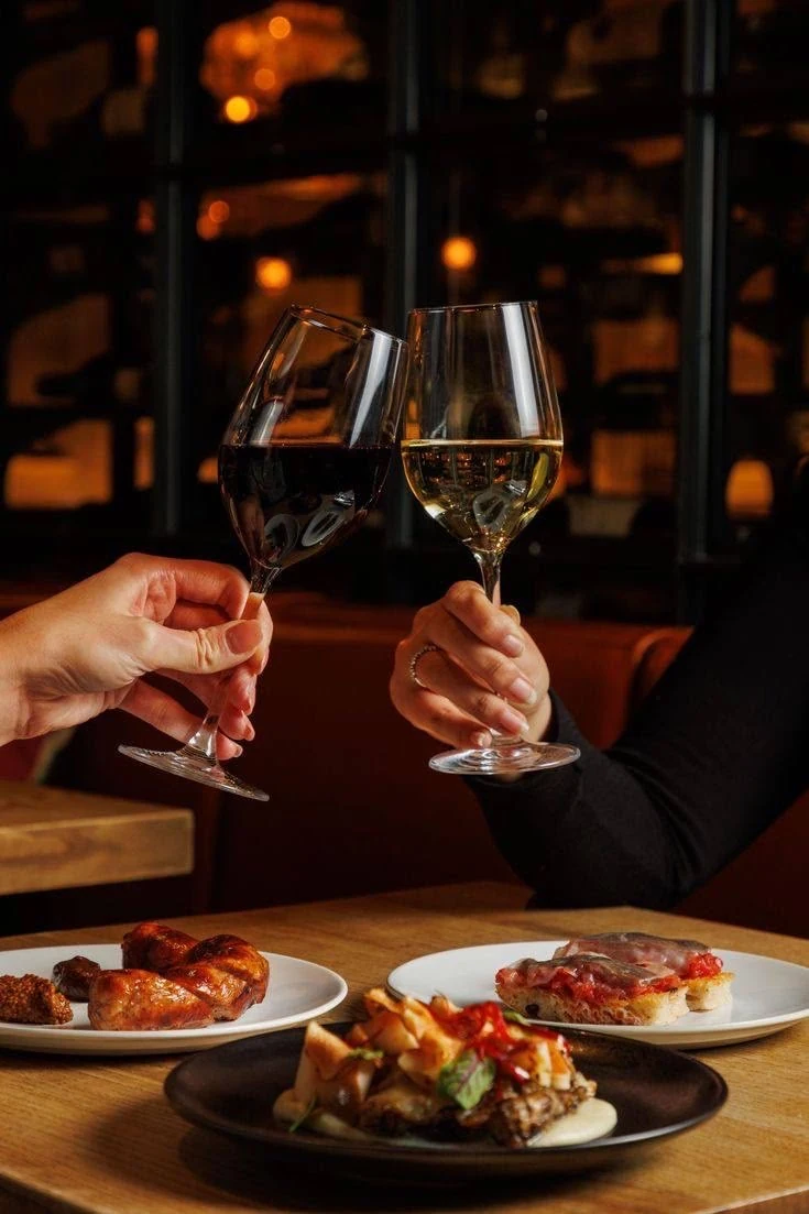 Dos personas brindan en una mesa con platos para compartir